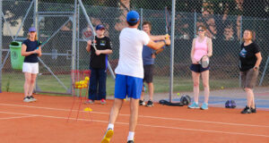 Coach Kevin Durney instructing a group of tennis players on a clay court.