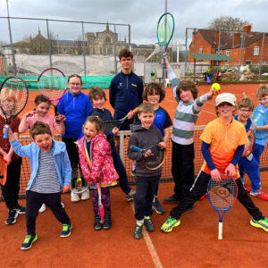 Big group picture of players posing in front of a net holding their rackets in the air