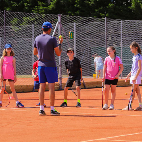 A coach talking to players on a clay court