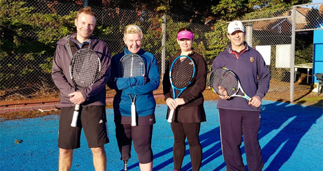 Wells A team Dave, Julia, Marie and Dave C posing for a team picture on a blue tennis court in the sunshine