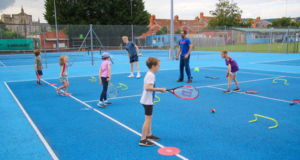 mini tennis kids practicing on a blue court with the coach